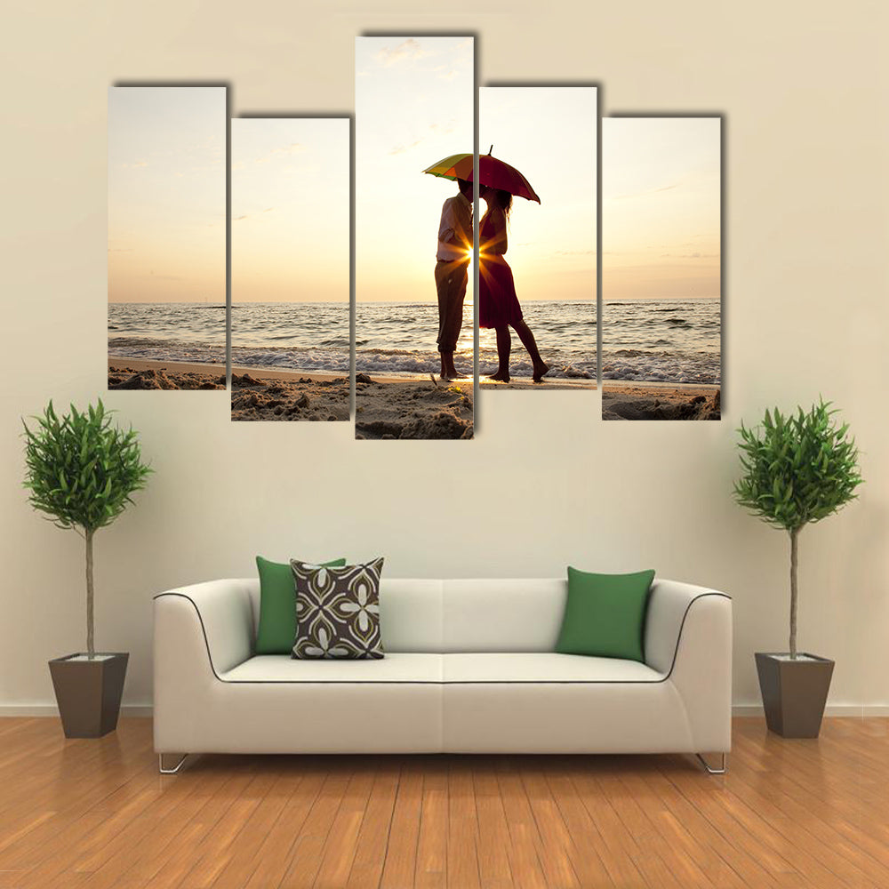 Couple kissing under umbrella at the beach in sunset multi panel canvas wall art