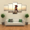 Couple kissing under umbrella at the beach in sunset multi panel canvas wall art