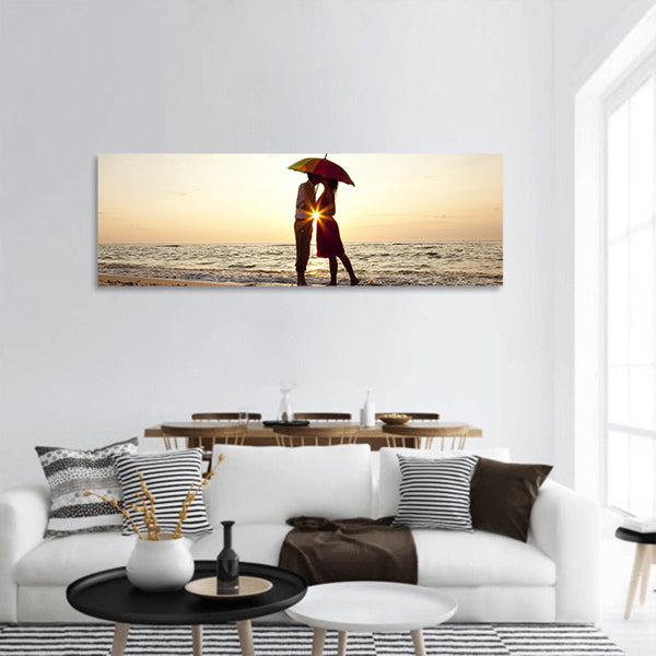 Couple kissing under umbrella at the beach in sunset panoramic canvas wall art