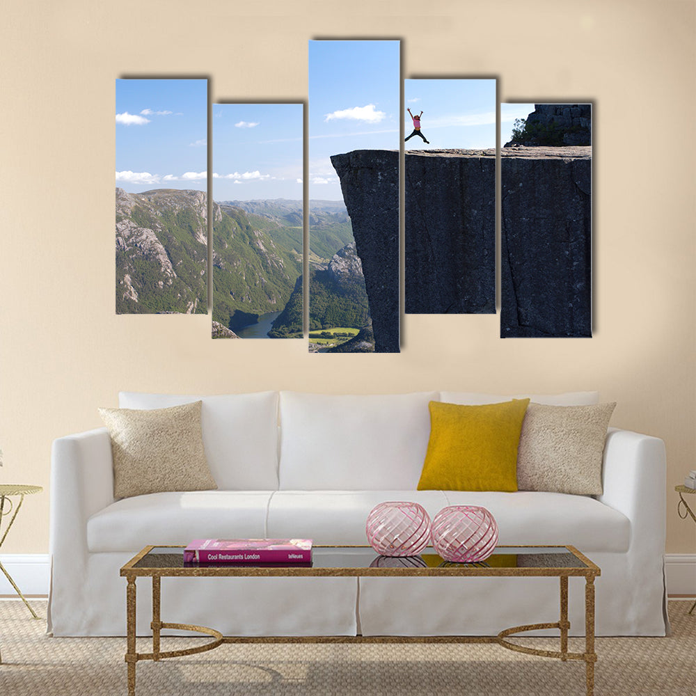 girl hiker jumping on Preikestolen, Preikestolen -famous cliff at the norwegian mountains Multi panel canvas wall art