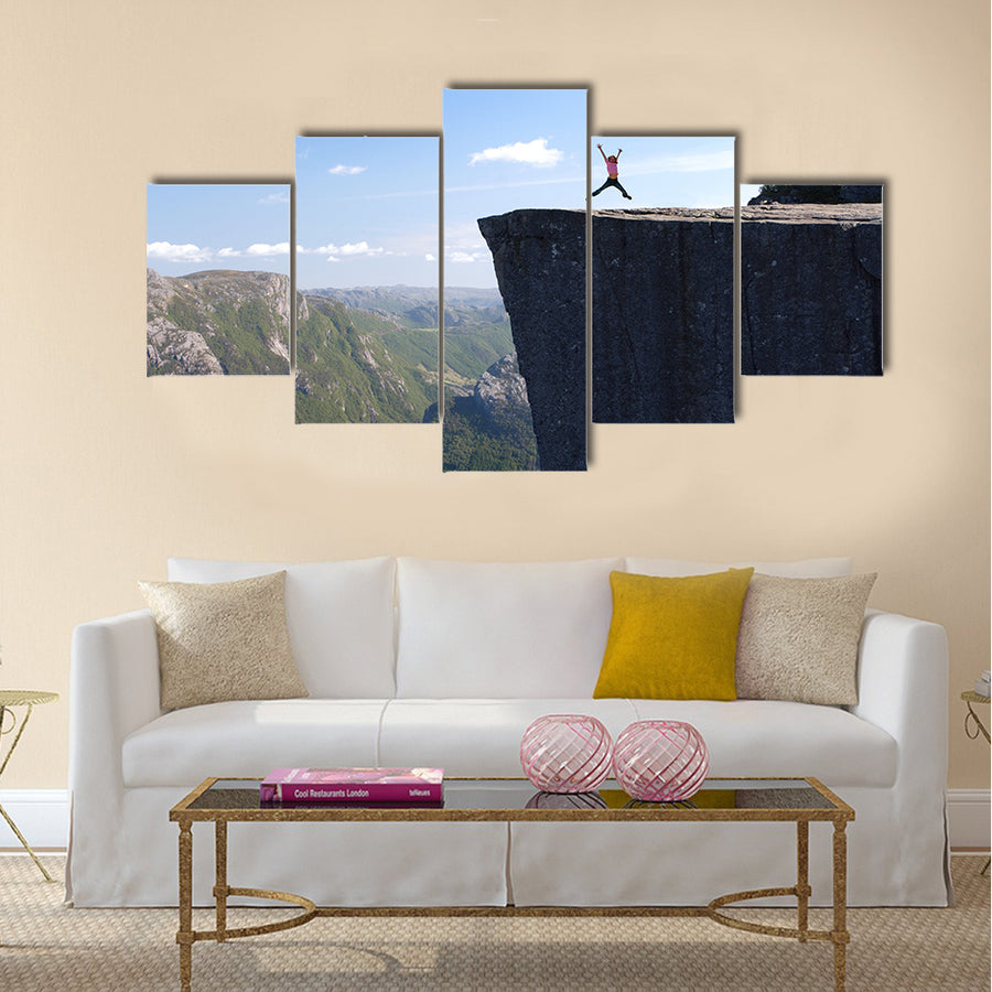 girl hiker jumping on Preikestolen, Preikestolen -famous cliff at the norwegian mountains Multi panel canvas wall art