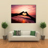 Silhouette hand in heart shape with sunrise in the middle and beach background multi panel canvas wall art