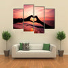 Silhouette hand in heart shape with sunrise in the middle and beach background multi panel canvas wall art