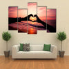 Silhouette hand in heart shape with sunrise in the middle and beach background multi panel canvas wall art