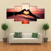 Silhouette hand in heart shape with sunrise in the middle and beach background multi panel canvas wall art