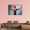 Young bodybuilder showing his biceps on a gray background Multi panel canvas wall art