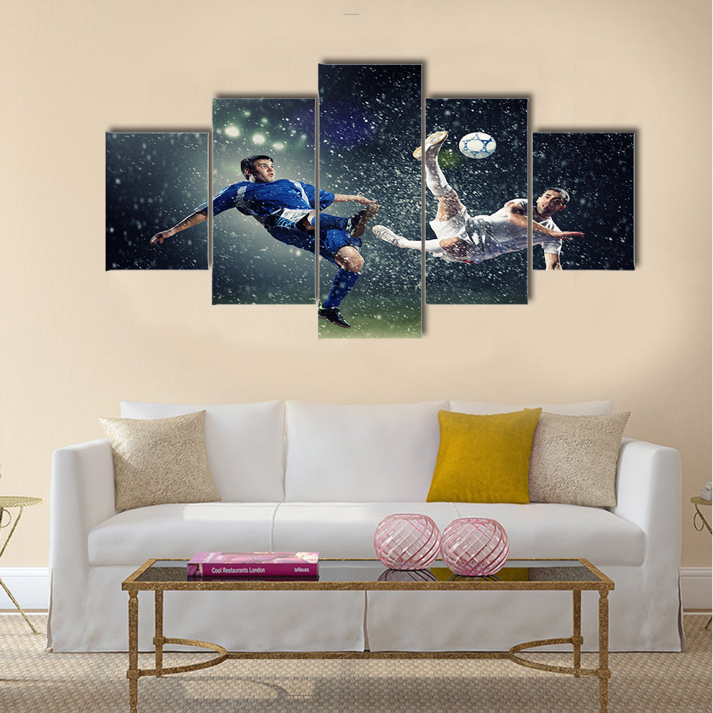 Two football players in jump to strike the ball at the stadium under rain Multi panel canvas wall art