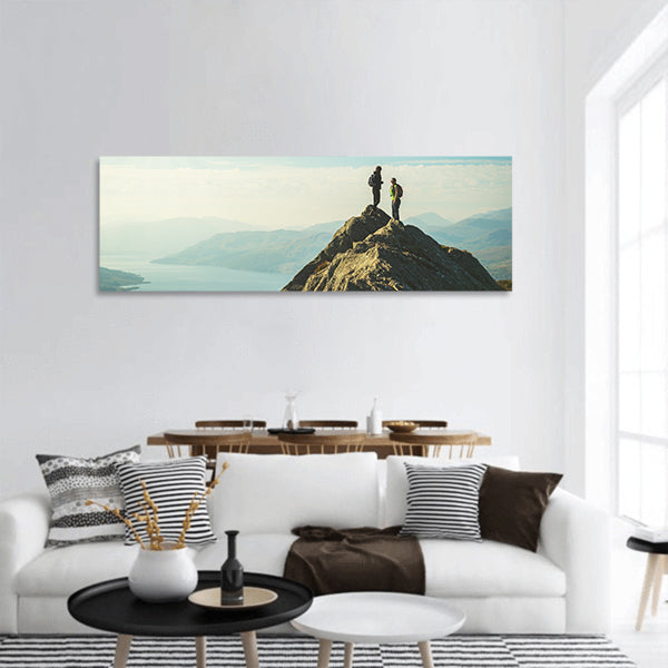 Two female hikers on top of mountain enjoying valley view, panoramic canvas wall art
