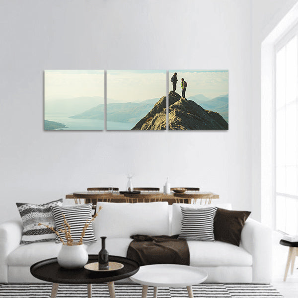 Two female hikers on top of mountain enjoying valley view, panoramic canvas wall art