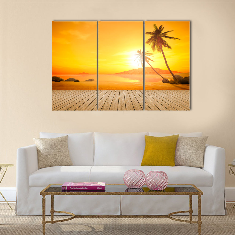 A beautiful sunset over the ocean with a palm tree and wooden jetty foreground Multi panel canvas wall art