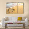 Heart drawn on the sand of a sea beach, soft wave and solar glare Multi panel canvas wall art