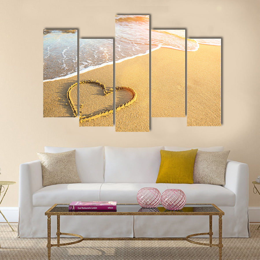 Heart drawn on the sand of a sea beach, soft wave and solar glare Multi panel canvas wall art