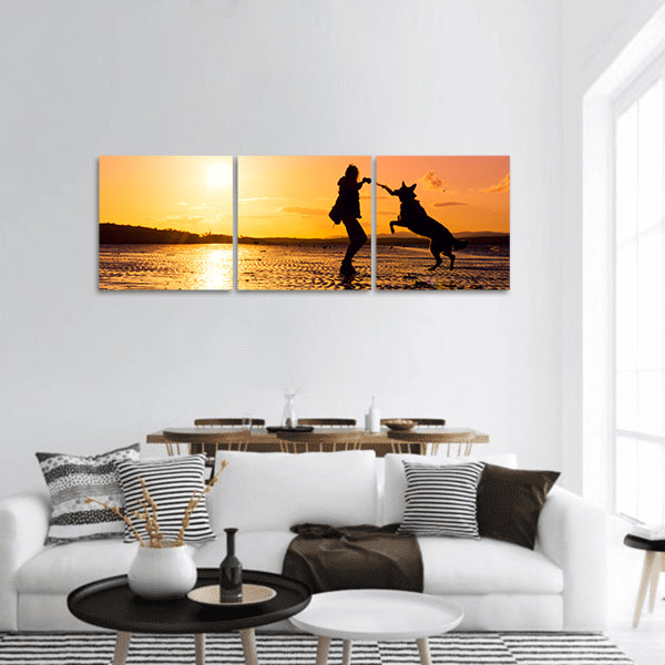 Hipster girl playing with dog at a beach during sunset, silhouettes panoramic canvas wall art