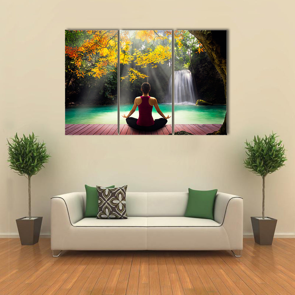Young woman in yoga pose sitting near waterfall Rear view