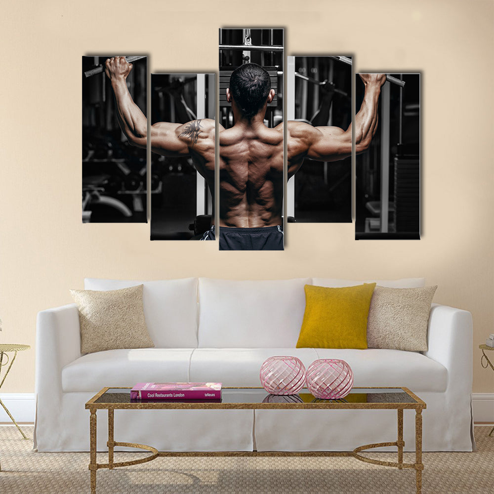 Athlete muscular bodybuilder training back on simulator in the gym, Multi panel canvas wall art