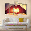 Heart shape making of hands against bright sea sunset multi panel canvas wall art