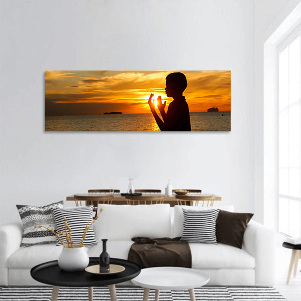 boy praying at sunset on the beach Panoramic Canvas Wall Art