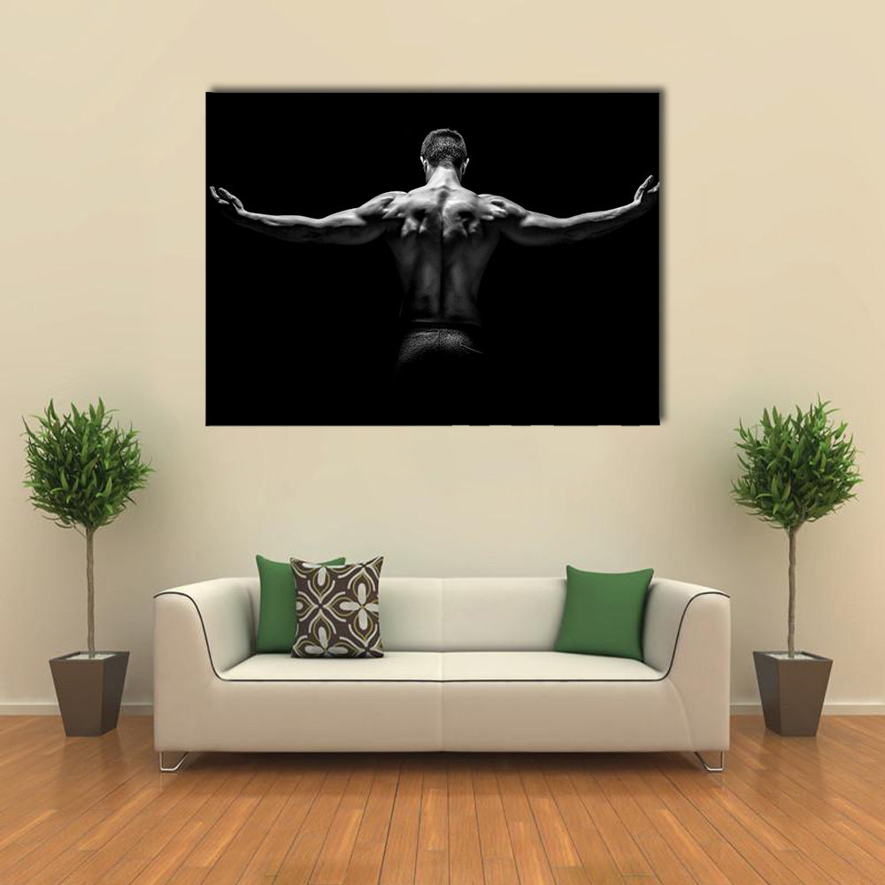 muscular young man with his arms stretched out on black background Multi panel canvas wall art
