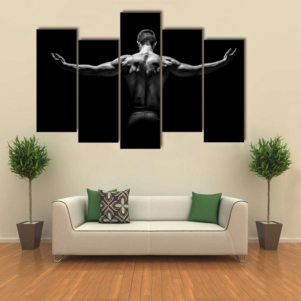 muscular young man with his arms stretched out on black background Multi panel canvas wall art