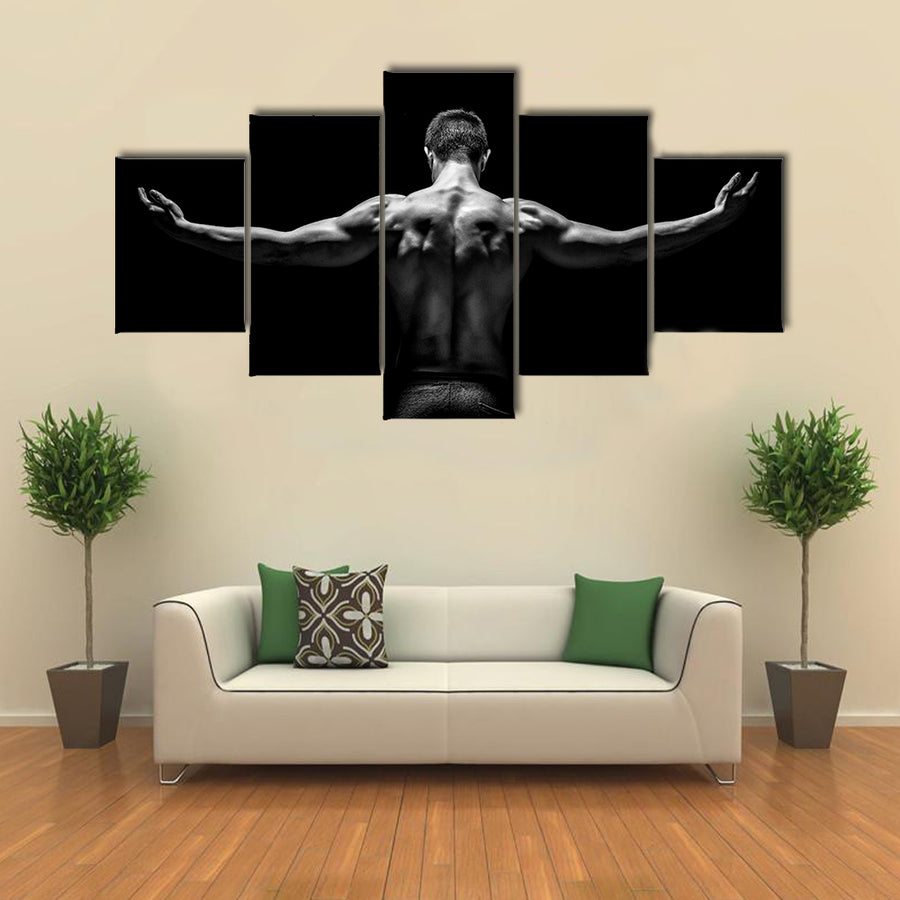 muscular young man with his arms stretched out on black background Multi panel canvas wall art