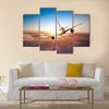 Commercial airplane flying above clouds in dramatic sunset light multi panel canvas wall art