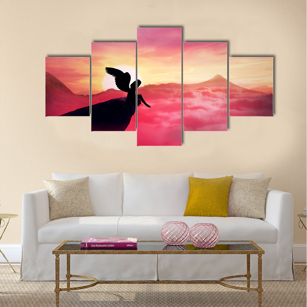 Silhouette of a lonely fallen angel with long wings standing on a cliff against a paradise sunset Multi Panel Canvas Wall Art