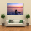 Silhouette of a yoga trainer balancing on the water on the paddle board over beautiful purple sunset Multi panel canvas wall art