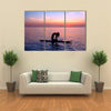 Silhouette of a yoga trainer balancing on the water on the paddle board over beautiful purple sunset Multi panel canvas wall art