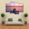 Silhouette of a yoga trainer balancing on the water on the paddle board over beautiful purple sunset Multi panel canvas wall art