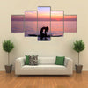 Silhouette of a yoga trainer balancing on the water on the paddle board over beautiful purple sunset Multi panel canvas wall art