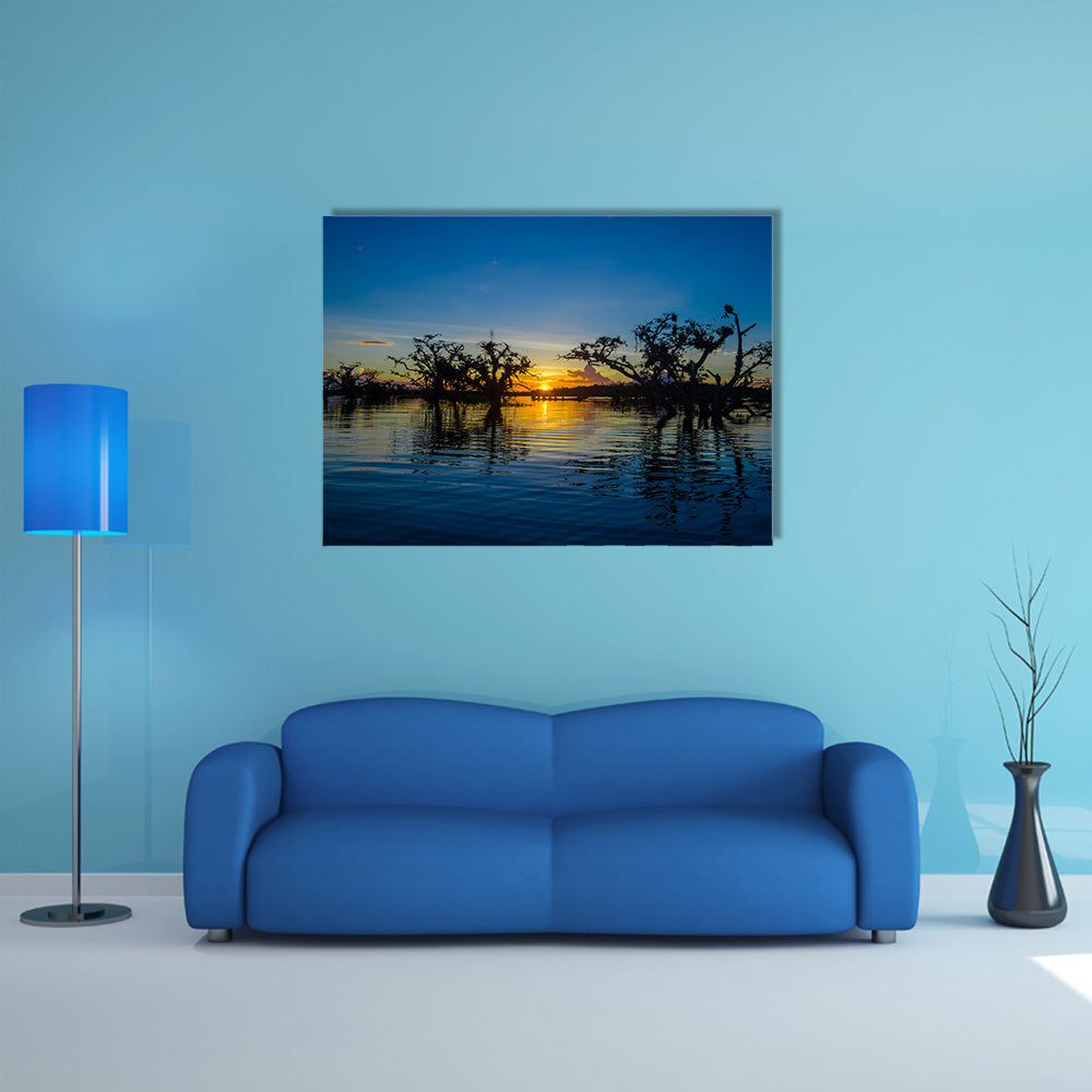 Trees silhouetted against an orange sky at sunset over Laguna Grande multi panel canvas wall art