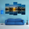 Trees silhouetted against an orange sky at sunset over Laguna Grande multi panel canvas wall art