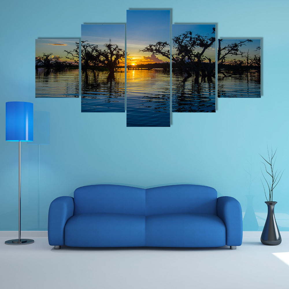Trees silhouetted against an orange sky at sunset over Laguna Grande multi panel canvas wall art