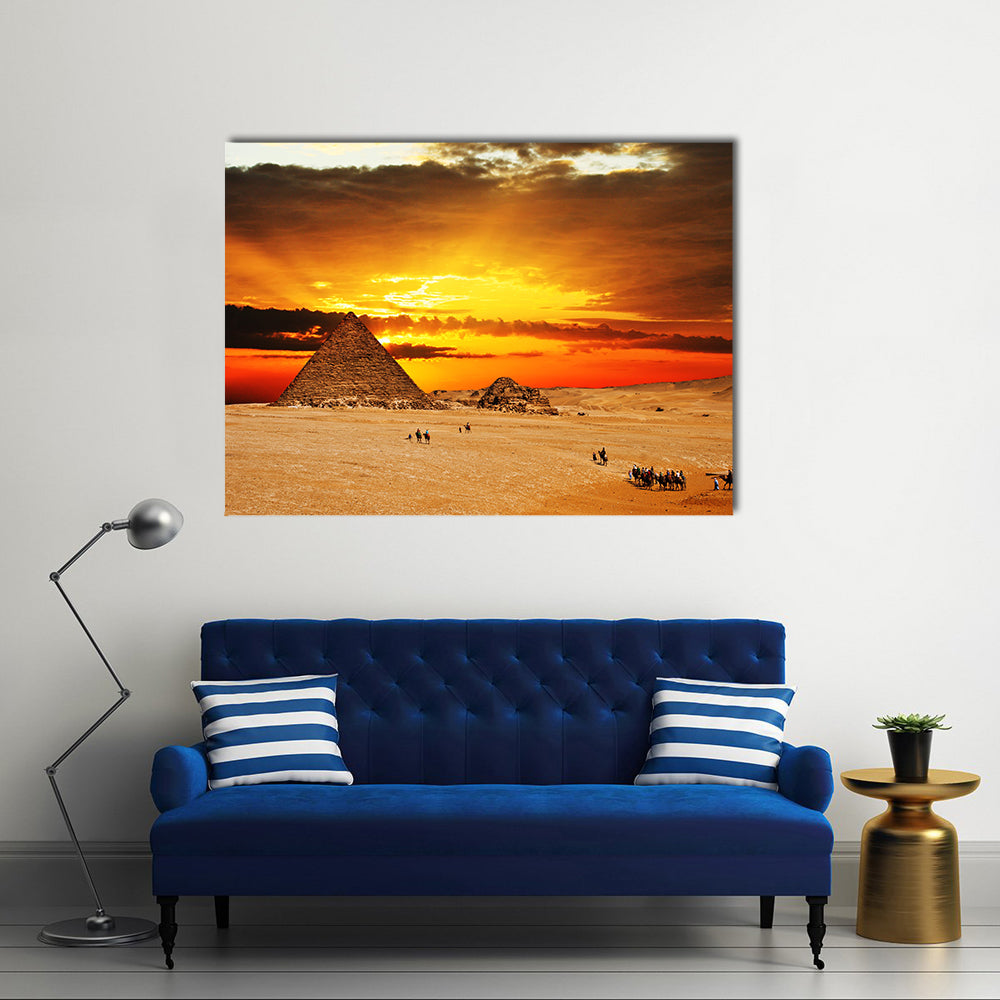 Camel caravan going through desert in front of pyramid at sunset Multi Panel Canvas Wall Art