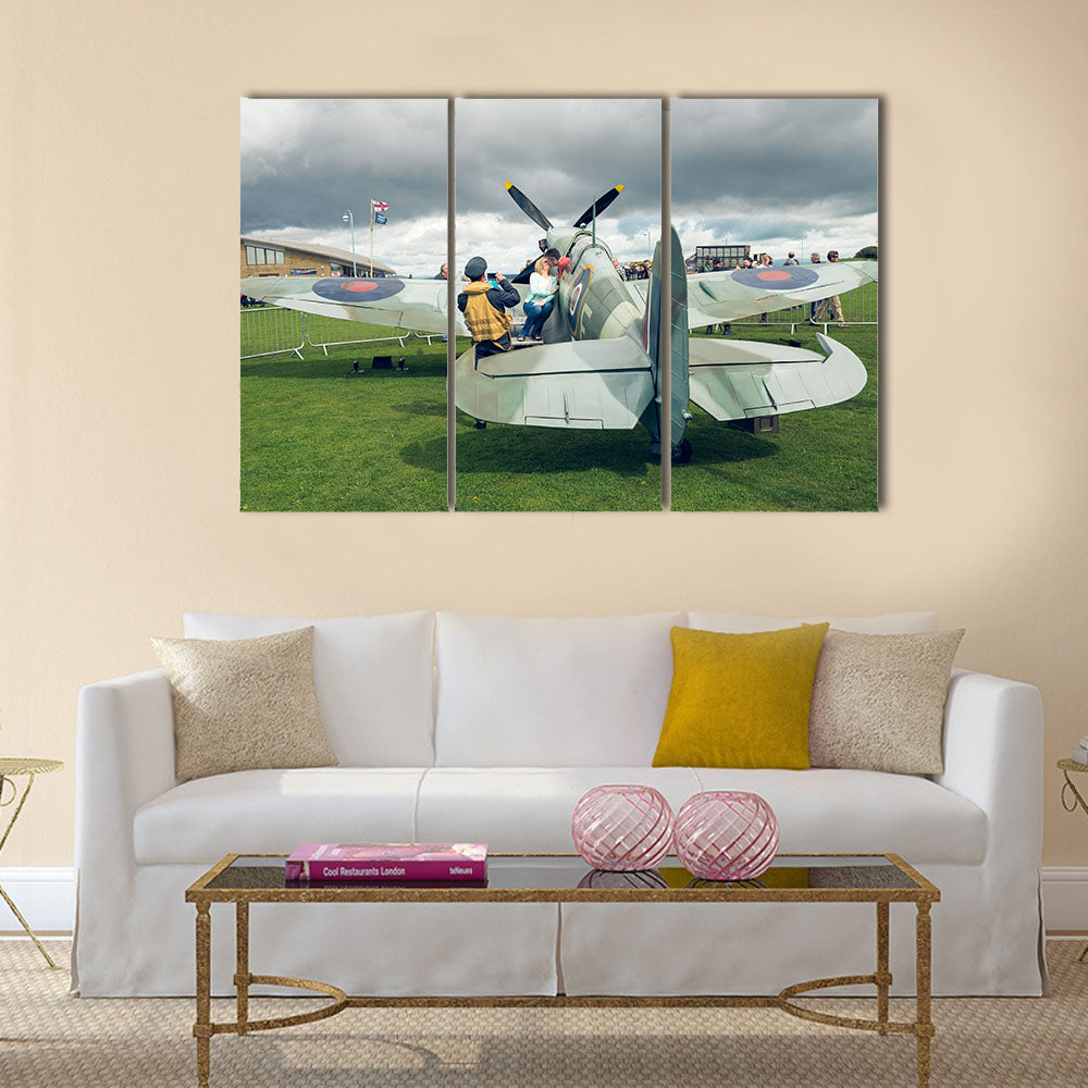 A full life size spitfire war plane replica with giant propellors, in a field on view to the public multi panel canvas wall art
