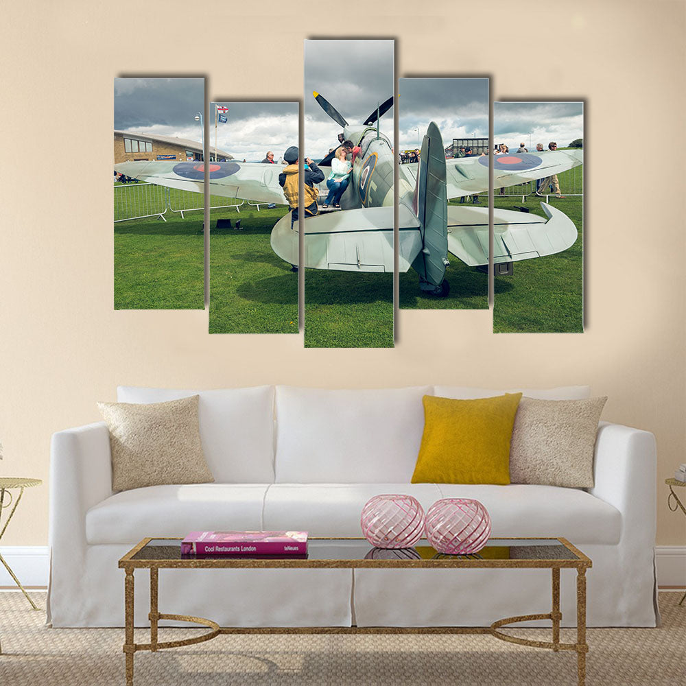 A full life size spitfire war plane replica with giant propellors, in a field on view to the public multi panel canvas wall art